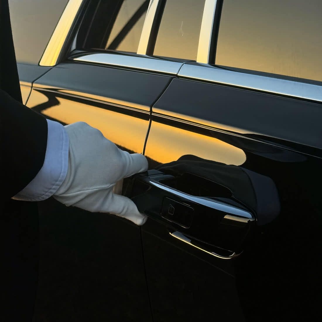 Chauffeur's white-gloved hand opening the rear door of a black luxury sedan